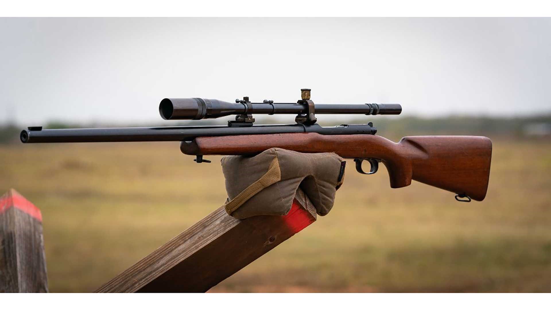 Winchester Model 70 rifle propped on sandbag with a grassy background.
