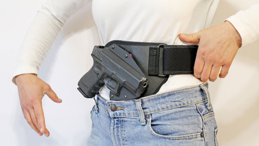 Woman in white shirt demonstrating a belly-band holster for a Glock pistol.