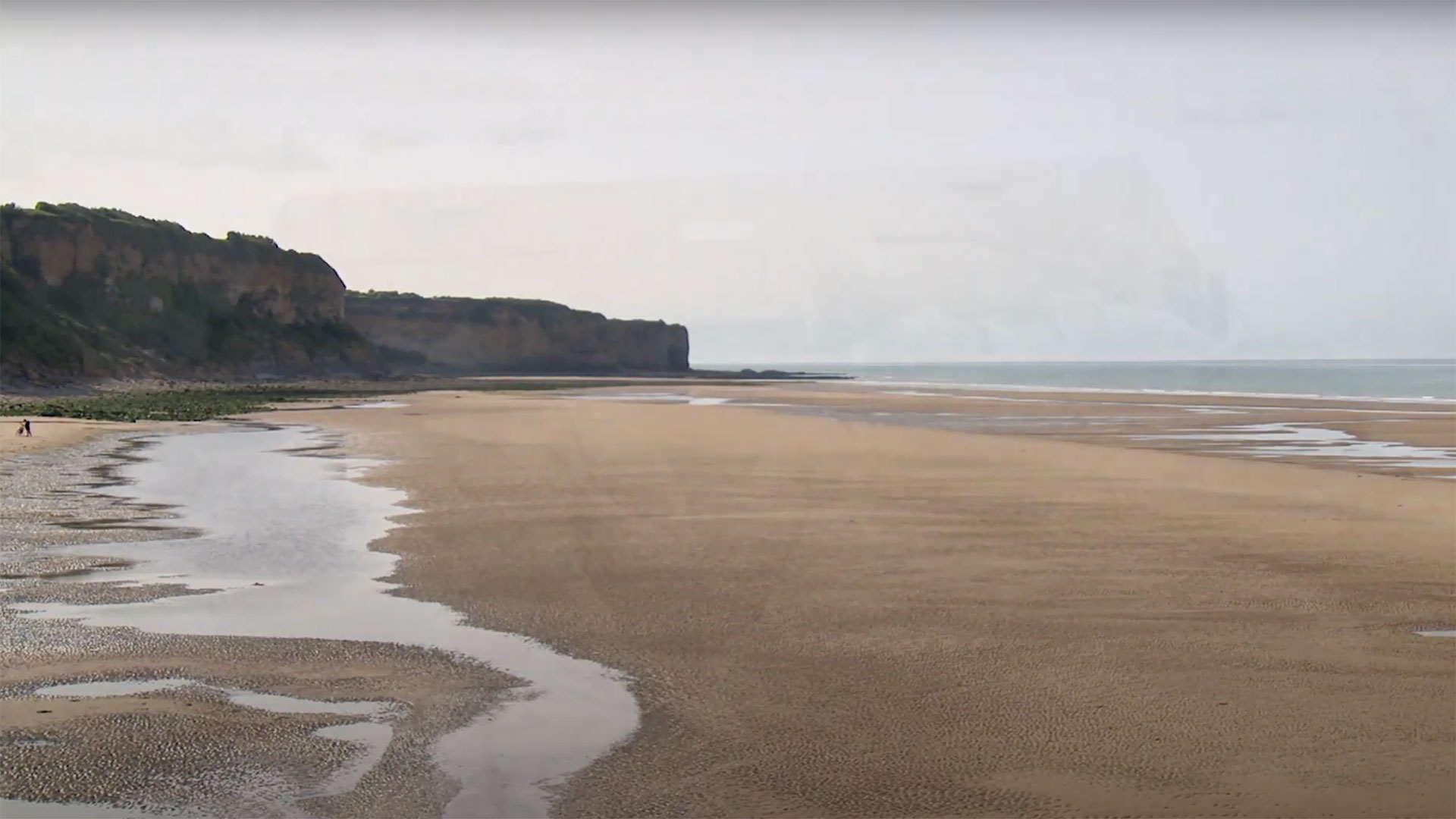 A view of Omaha beach today, showing the outlay of the bluffs and the long stretch of sand that separates them from the shoreline.