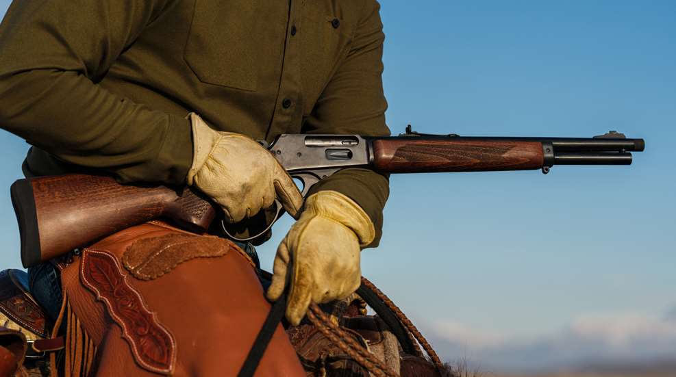 Rossi lever-action rifle held in hand of cowboy on horse blue sky
