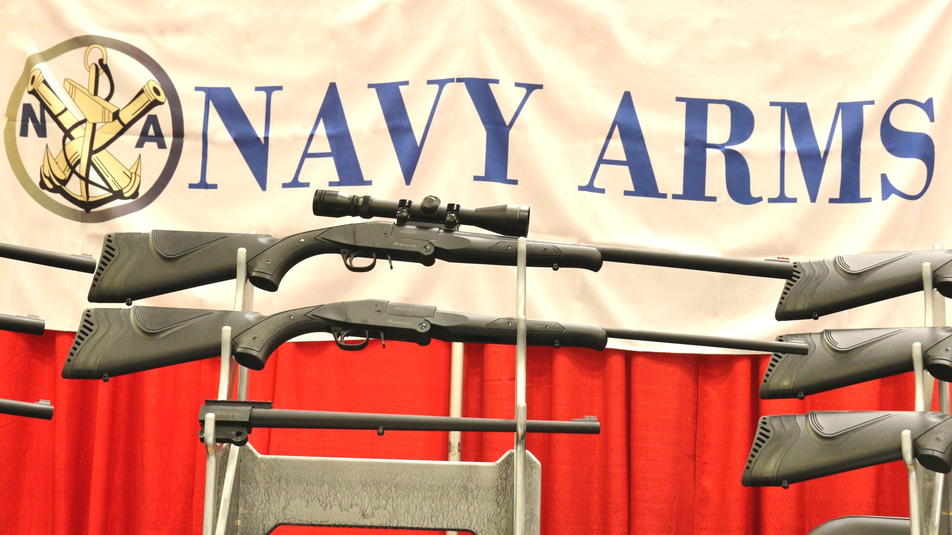 Navy Arms Midland single-shot rifle shotgun on rack showing modularity comparison banner background