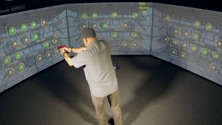 Man with firearm practicing with a digital simulation screen surrounding.