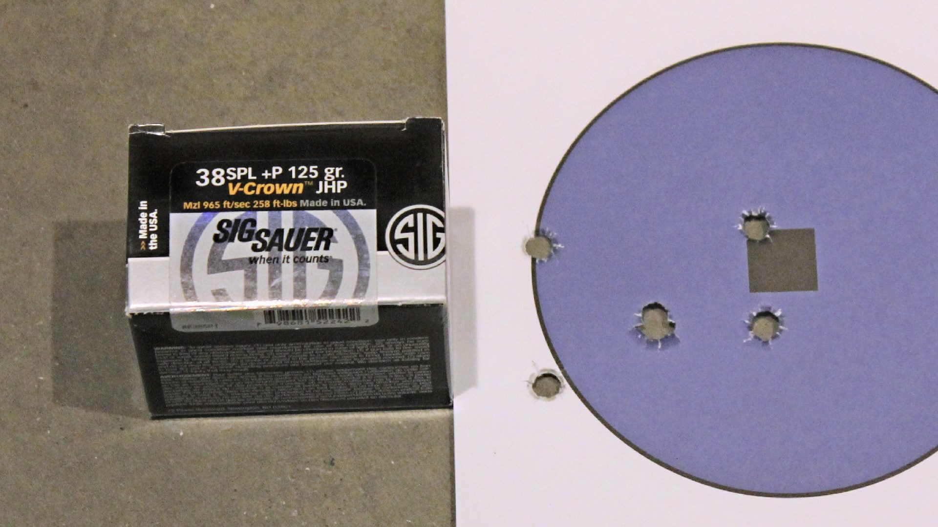 A box of SIG Sauer .38 Special ammunition next to a round purple target with bullet holes.