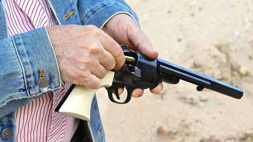 Man in blue demin coat with white-stripped shirt loading Uberti Wild Bill 1851 Navy Conversion.