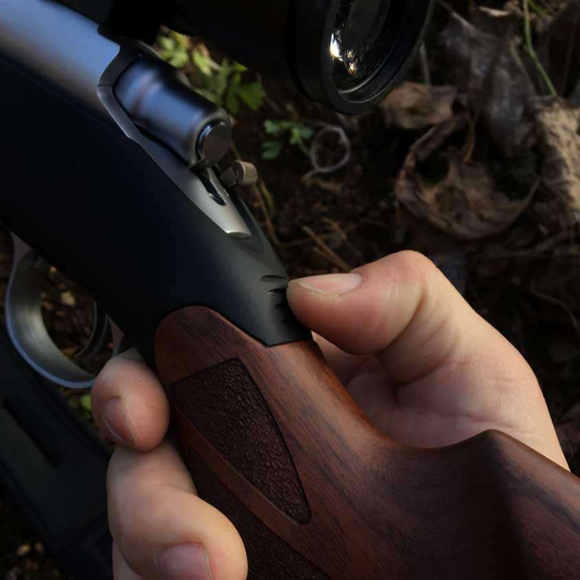 Rifle with wood stock in hand with closeup on thumb and black metal.