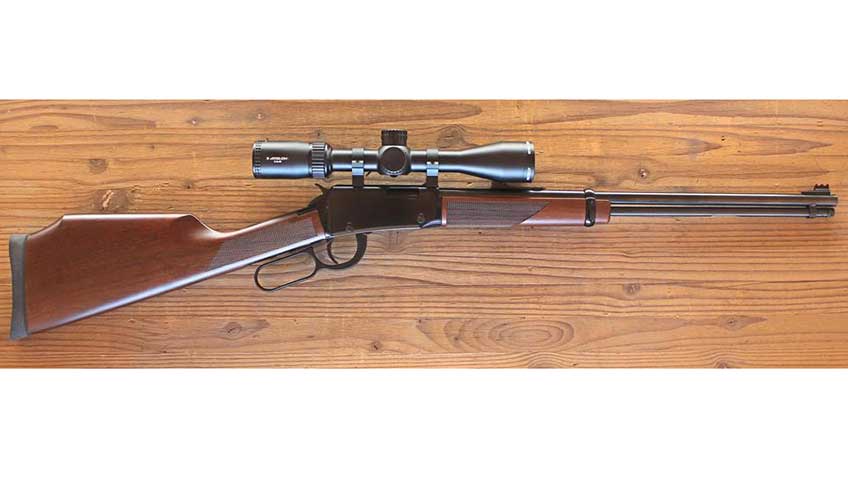 Right-side view of Henry Repeating Arms Varmint Express lever-action rifle with scope attached laying on wooden table.