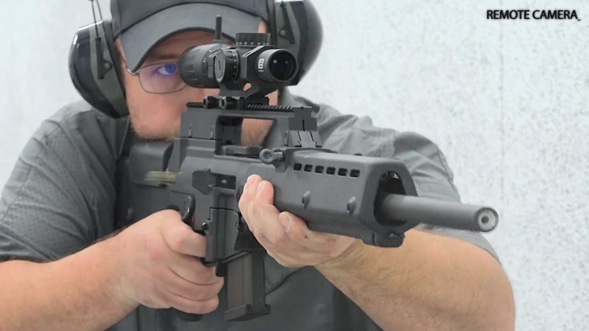 Man wearing gray polo hat earmuff on range shooting black H&K SL8-6 semi-automatic rifle dynamic angle remote camera
