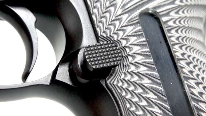 Close-up view of pistol's magazine release and trigger shown on white background.