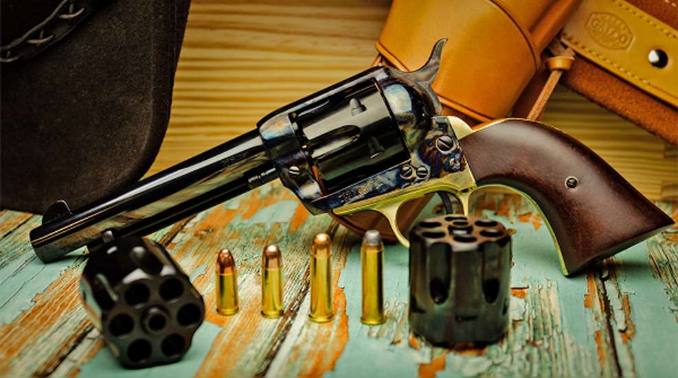 Pietta's 1873 single-action revolver on a wood deck, shown with two extra cylinders and four compatible cartridges.