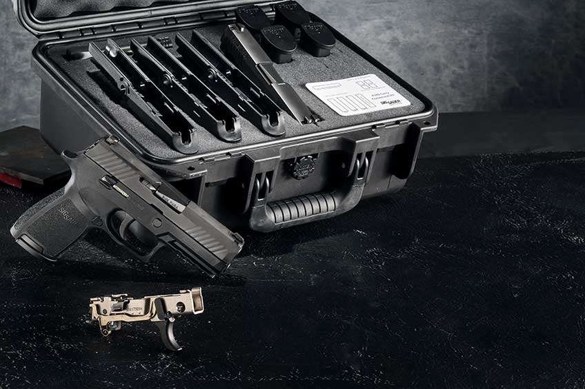 SIG Sauer P320 shown on a black background alongside a hard-sided case filled with grip frames and a serialized metal chassis.