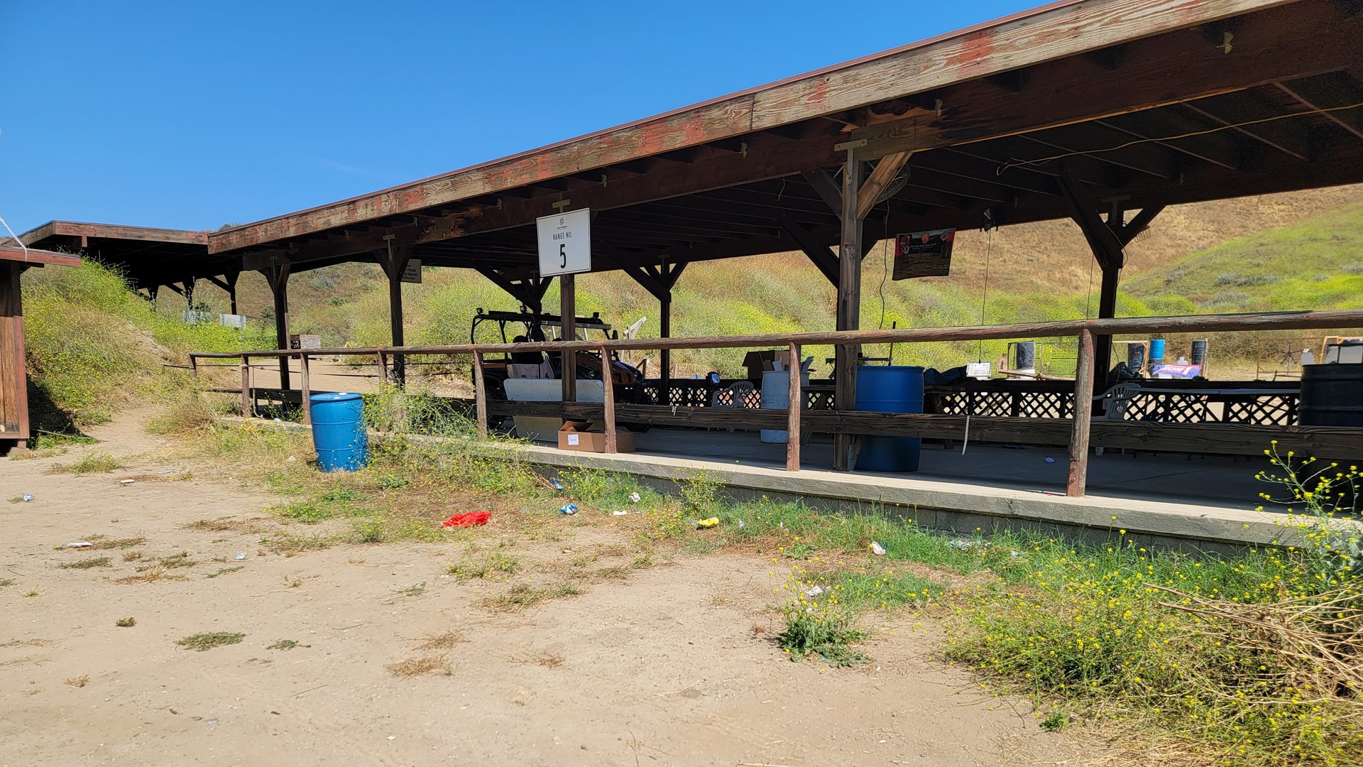 Outdoor shoooting range covered benches facility mountain backdrop wood blue barrels grass