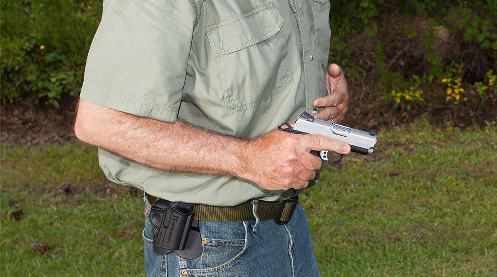Man with pistol drawn from holster signifying self-defense scenario outdoors