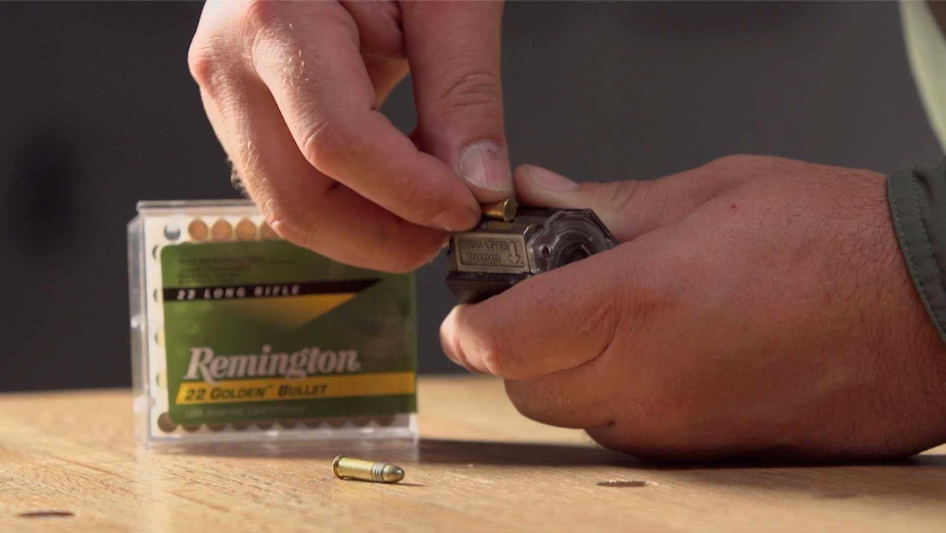 Hands showing a single round of Remington .22 Long Rifle being pushed into the T/CR22 rotary magazine.