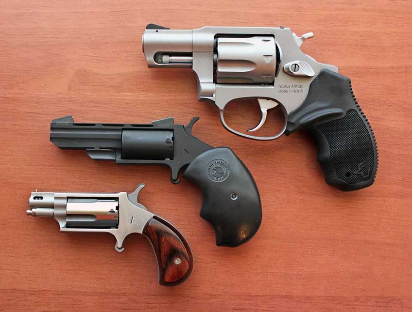 arrangement three revolvers guns pistols handguns on table stainless steel black wood table