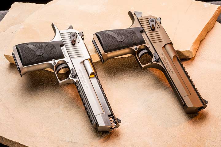 Two Magnum Research Desert Eagles lay side-by-side on a sandstone background; one is all stainless-steel and the other features a tan Cerakote finish.