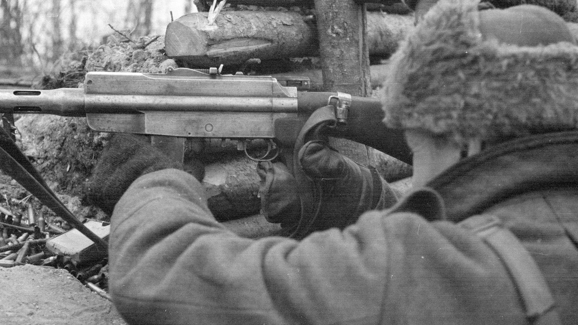 Over-the-shoulder view of Finnish soldier wearing mittens firing M/26 light machine gun foxhole