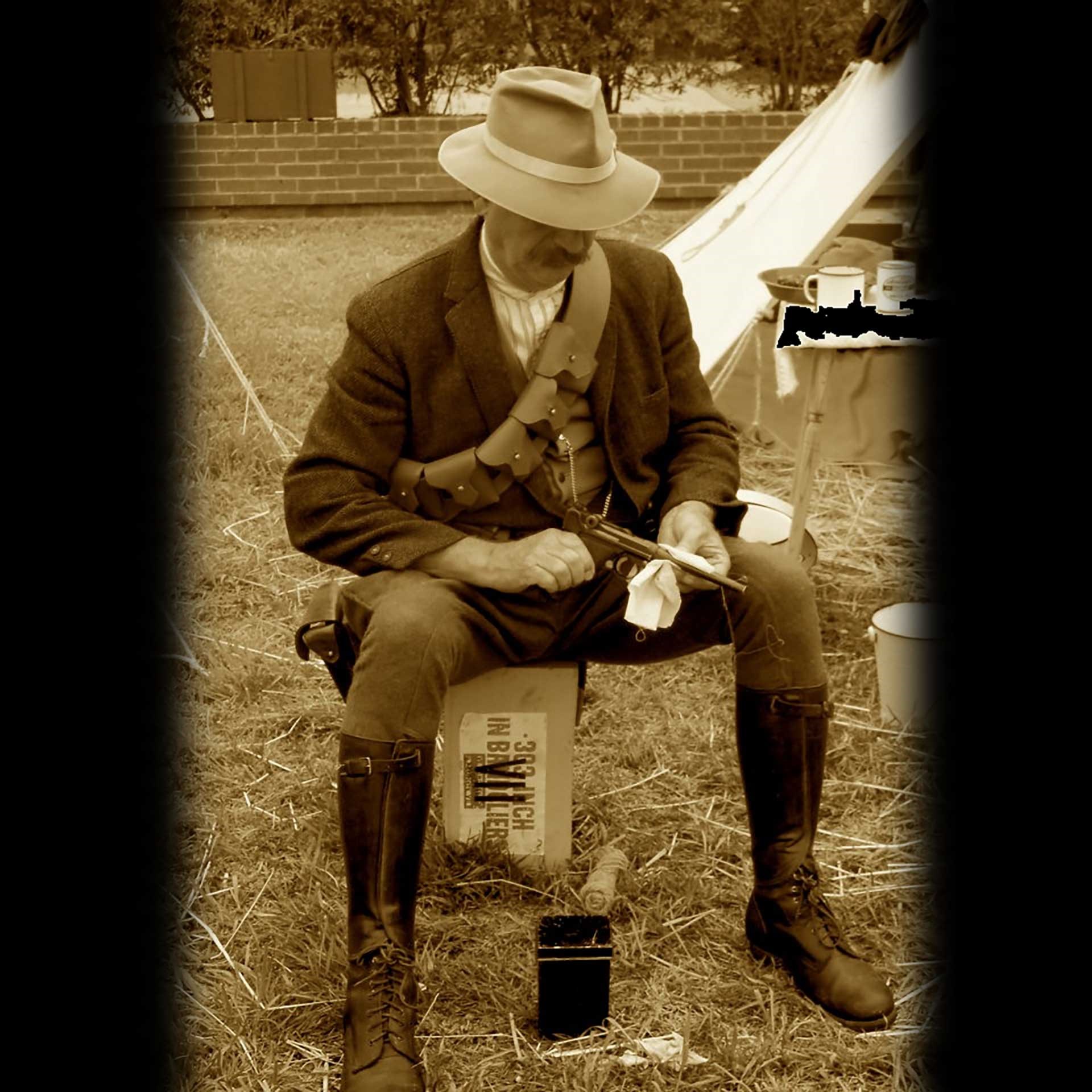 A man sitting on a wooden box, cleaning his Luger pistol in a campsite.