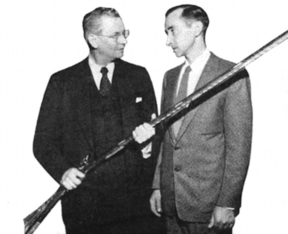 black and white photo two men suits holding rifle gun musket