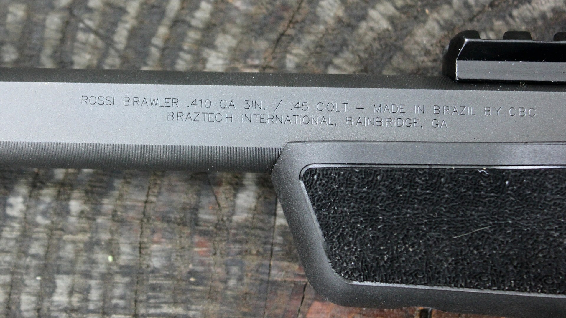 Rossi Brawler barrel close-up view stamping words engraved in metal company information gun information black metal black polymer Picatinny rail on wood log rings