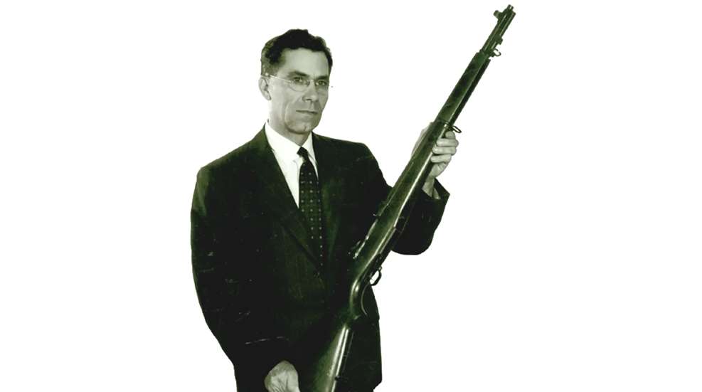 John C. Garand portrait wearing coat and tie holding M1 Garand rifle with wood stock