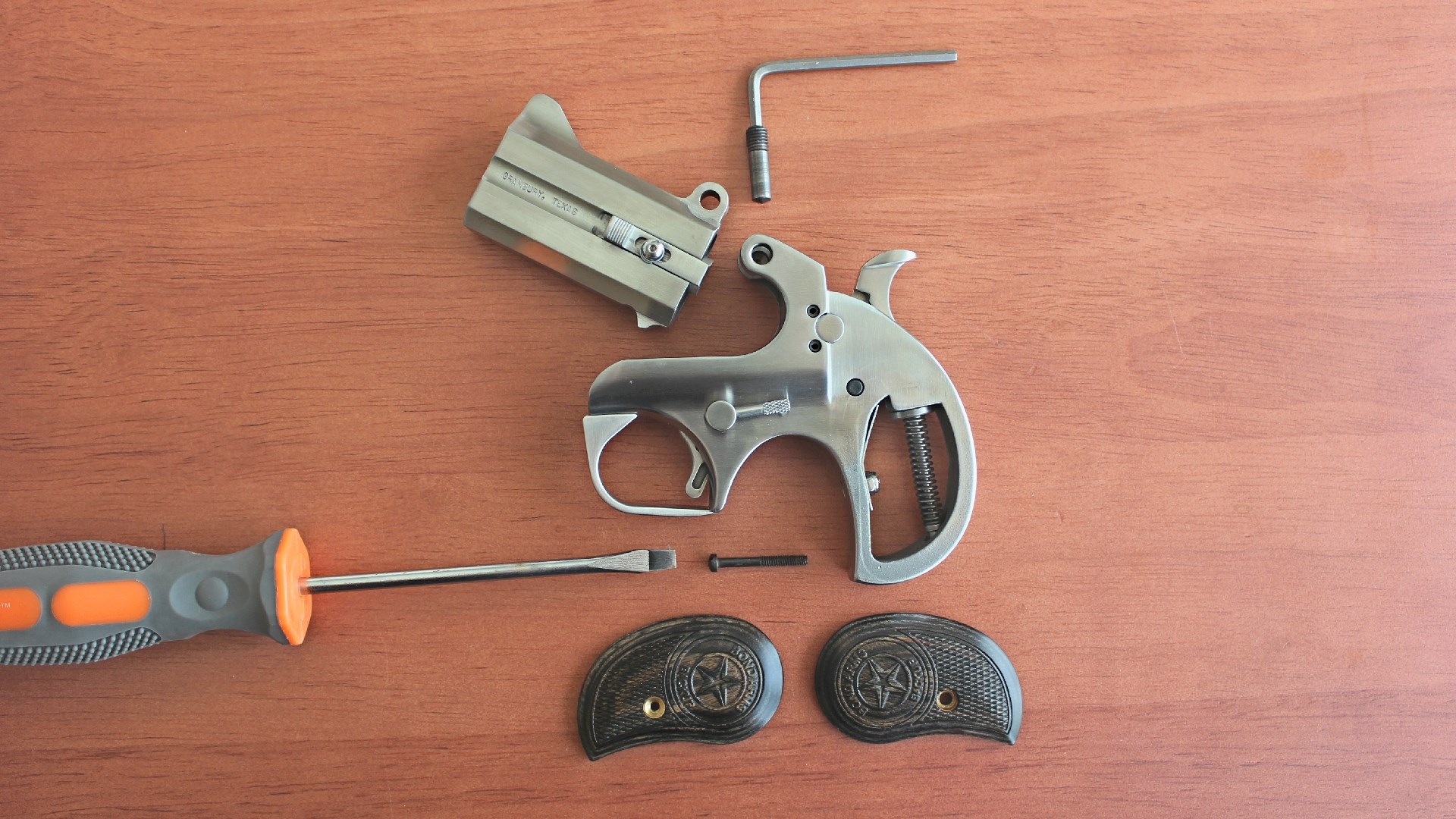 A disassembled Bond Arms derringer on a wood table surface.