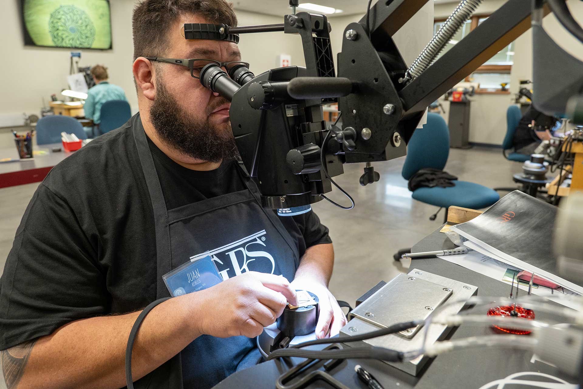 A man learns to engrave a metal plate in a classroom environment.