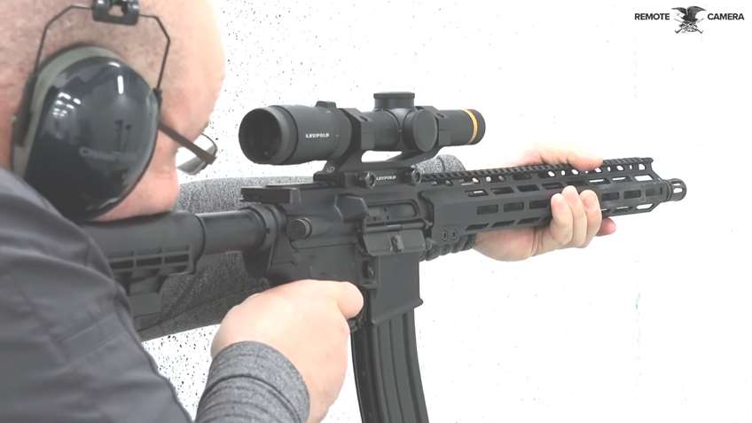 Man bearing down on black-colored rifle on white shooting range.