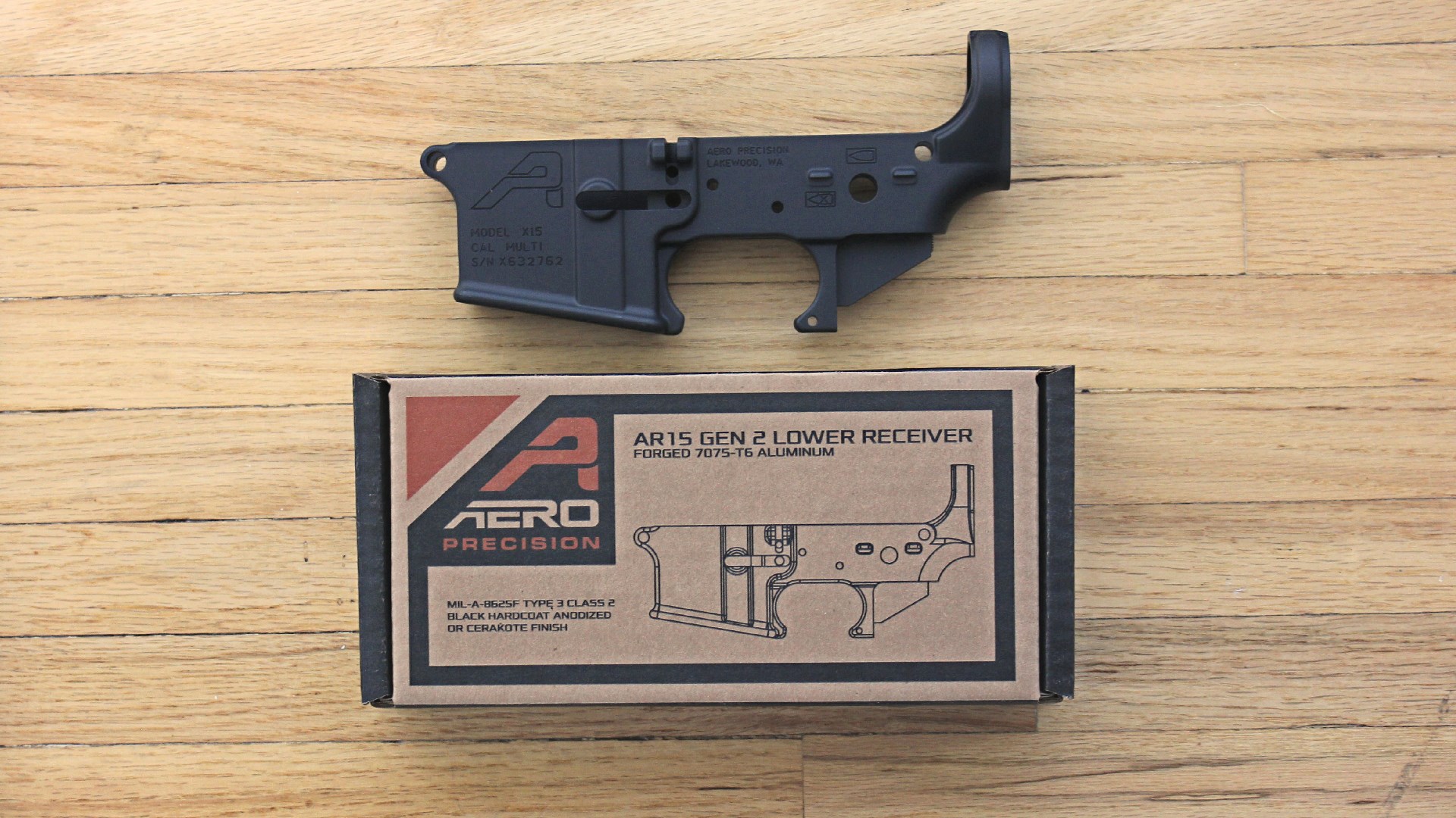 Aero precision lower receiver left-side view black metal gun part shown with cardboard box on wood flooring