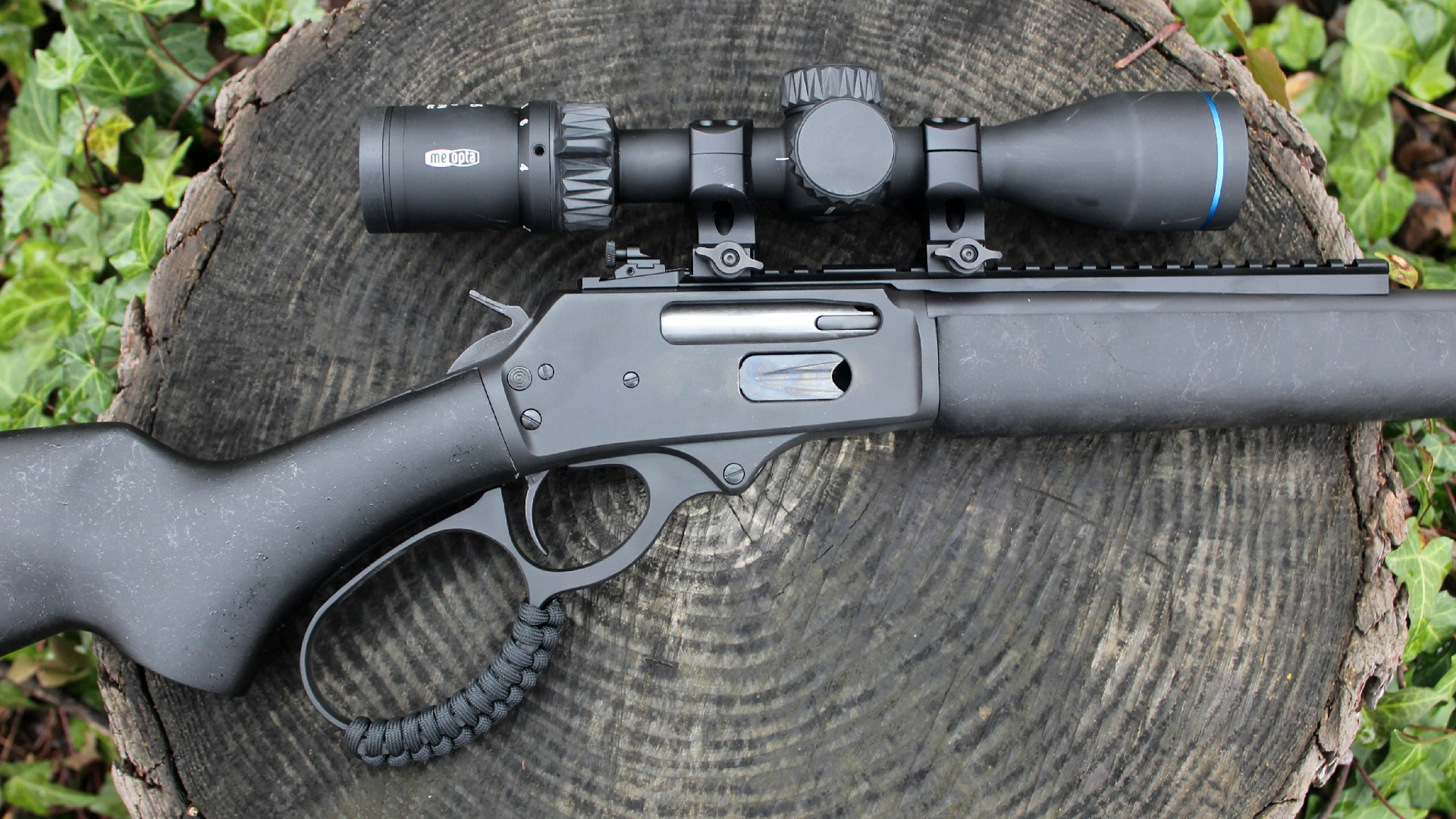 Rossi R95 Triple Black lever-action rifle receiver closeup lever loop riflescope rear sight right-side action shown on log stump green ivy background